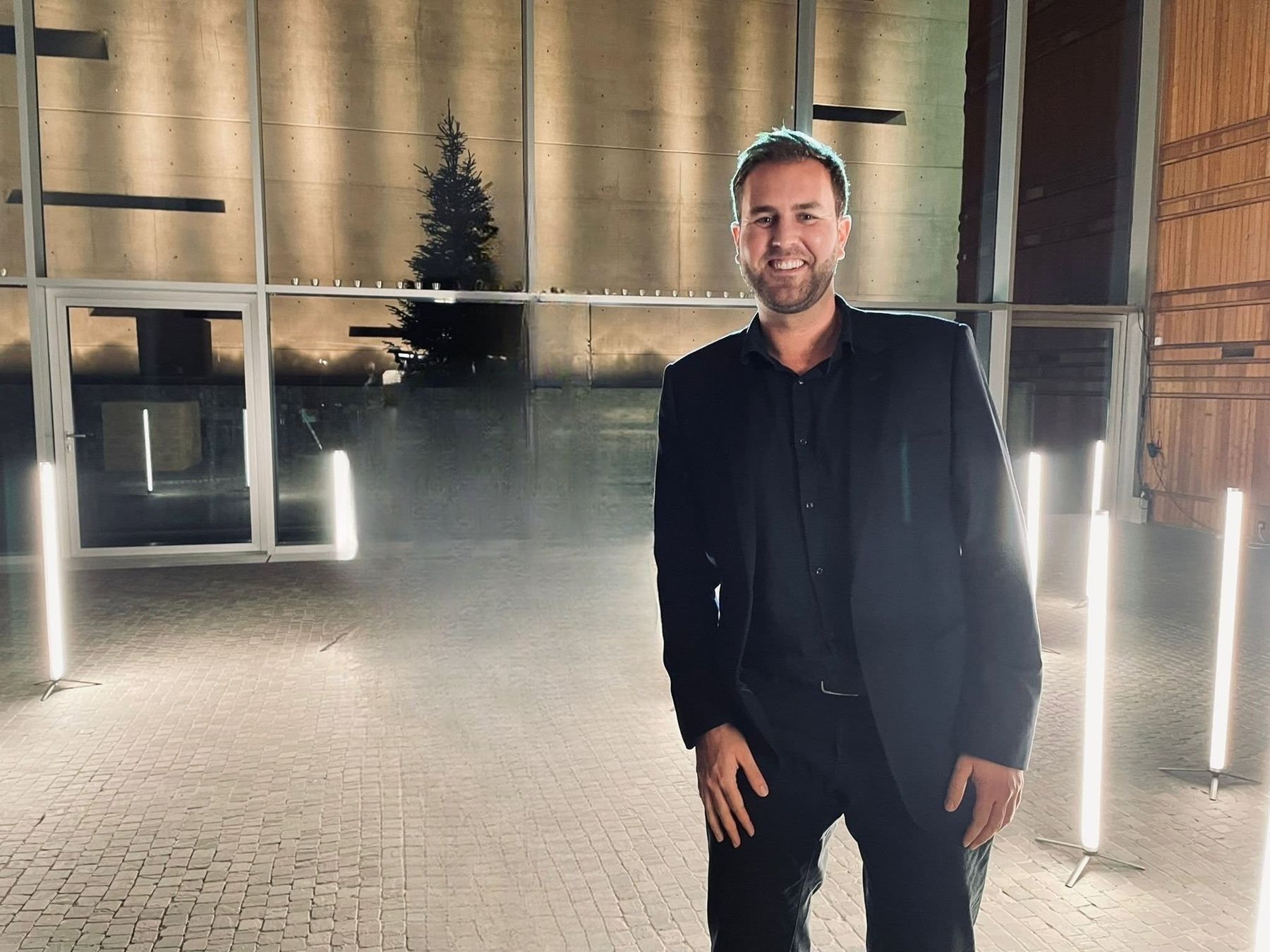 Philipp Quiring im dunklen Sakko vor einer beleuchteten Betonwand